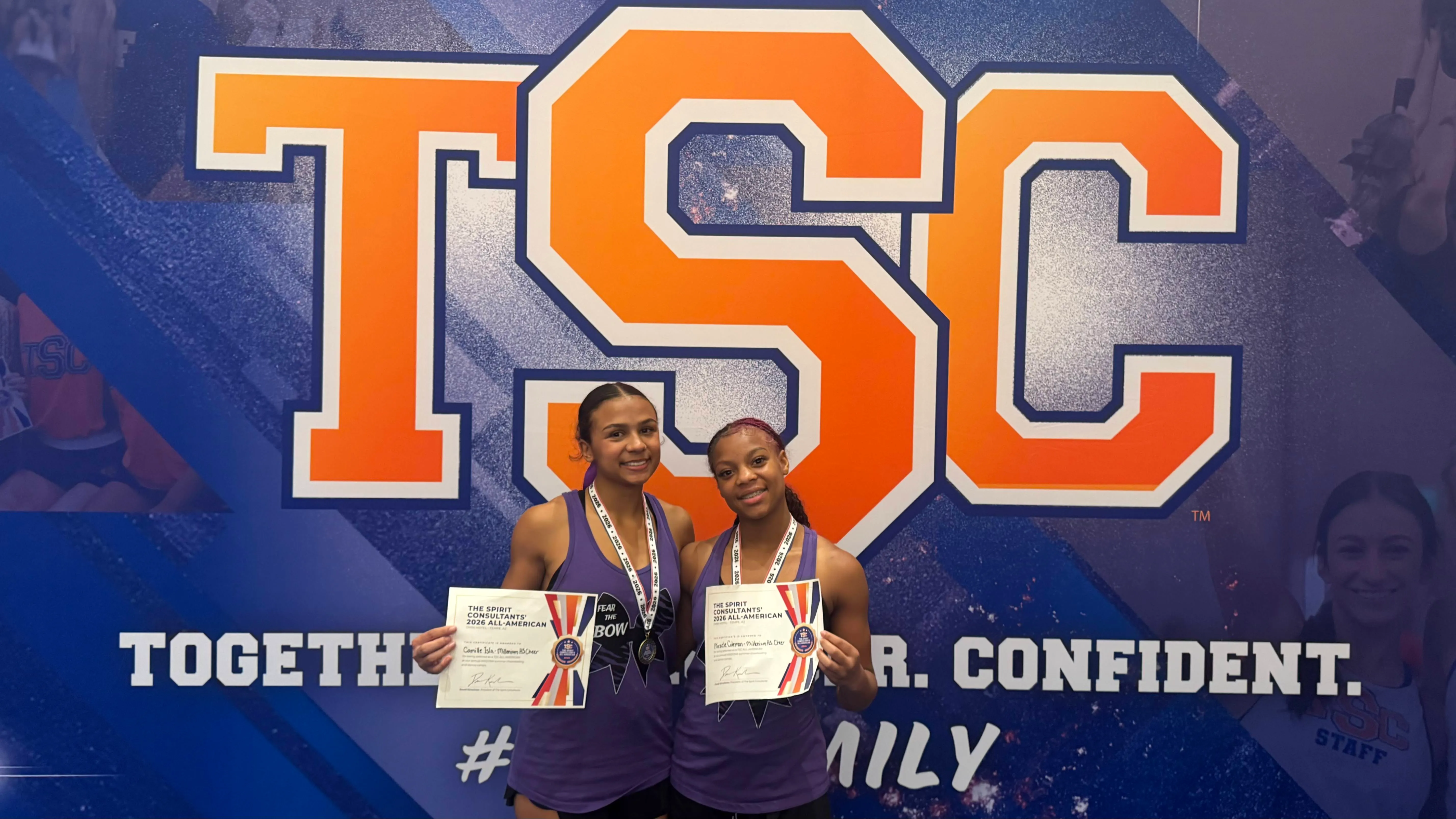 Two Millennium Tigers cheerleaders holding their 2026 TSC All-American certificates in front of the TSC banner